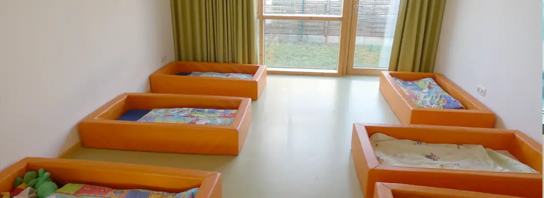Ruheraum im Familienzentrum Vierlinden mit mehreren niedrigen Kinderbetten und großen Fenstern zum Außengelände.